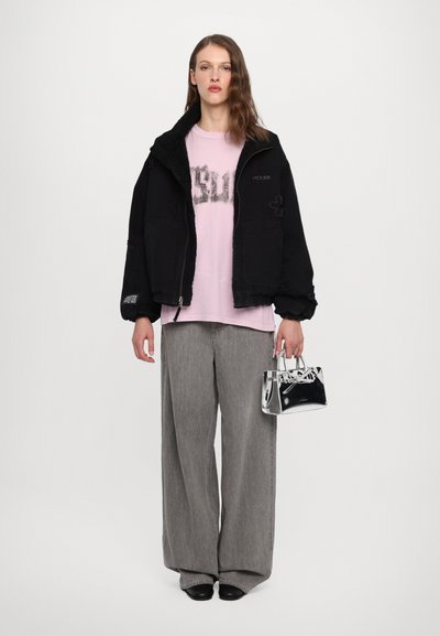 Black sherpa-lined jacket over a pink graphic t-shirt, paired with gray wide-leg pants and a small transparent handbag.