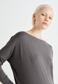 Gray long-sleeve top with a loose fit, wide neckline, and soft texture. The fabric drapes smoothly over the shoulders and upper arms.