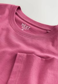 T-shirt rose ajustée en coton. Présente un col rond et une poche poitrine. Texture lisse avec des détails de couture soignés.