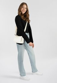 Blazer nero su una maglietta nera, jeans blu chiaro e sneakers bianche. Una borsa a tracolla bianca presenta un design curvo e hardware argentato.