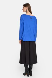 Niebieska bluzka z długim rękawem i szerokim dekoltem, luźny krój, z małą metką z tyłu, w połączeniu z czarną długą spódnicą i kozakami za kolano.