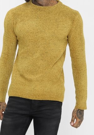 Senfgelb gestrickter Pullover mit rundem Halsausschnitt, strukturiertem Muster und langen Ärmeln, kombiniert mit dunklen Jeans.