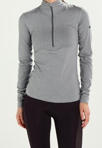 Harmaa, pitkähihainen urheilu paita, jossa on neljänneksen vetoketju ja slim fit -leikkaus; yhdistetty mustiin legginsseihin, joissa on tekstuuripaneelit.