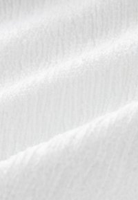Drapé en tissu éponge blanc avec une surface texturée, présentant des fibres douces et surélevées dans un motif ondulé. Un reflet de lumière subtil met en valeur la texture.
