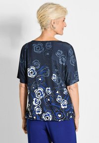 Marineblauw bloemenblouse met zachte textuur en brede mouwen, versierd met blauwe en witte rozenpatronen; gecombineerd met blauwe broeken.