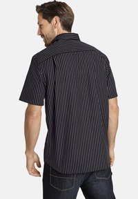 Schwarzes Kurzarmhemd mit weißen senkrechten Streifen, ausgestattet mit einem spitzen Kragen und einer Knopfverschluss-Rückseite. Aus glattem Baumwollstoff.