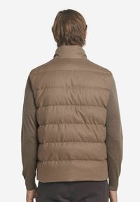 Braune Steppweste mit hohem Kragen, horizontalen Steppnähten, gesteppter Textur und weichem Stofffinish.