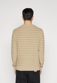 Beige gestrickter Pullover mit horizontalen Streifen, rundem Ausschnitt, langen Ärmeln und gerippten Bündchen. Verfügt über ein kleines Logolabel am Saum.