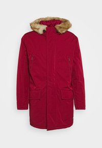 Röd parkajacka med en fuskpälsfodrad huva, två framfickor och en ficka med dragkedja på sidan. Tillverkad av ett slätt, väderbeständigt material.