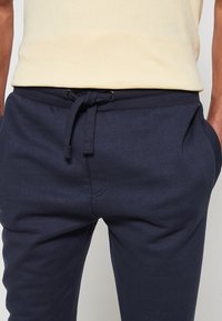 Navyblauwe sweatpants van zachte stof, met een trekkoord in de taille, zijzakken en een gladde textuur. Eenvoudig, casual ontwerp.