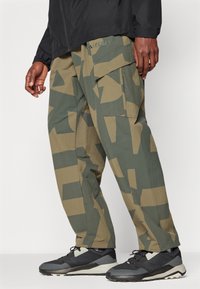Cargo pants in a camouflage pattern with shades of green and beige. Features multiple pockets and a straight-leg design.