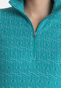 Türkisfarbener Pullover mit hohem Kragen, der ein weißes geometrisches Muster aufweist. Enthält einen teilweisen Reißverschluss und eine strukturierte Stoffoberfläche.