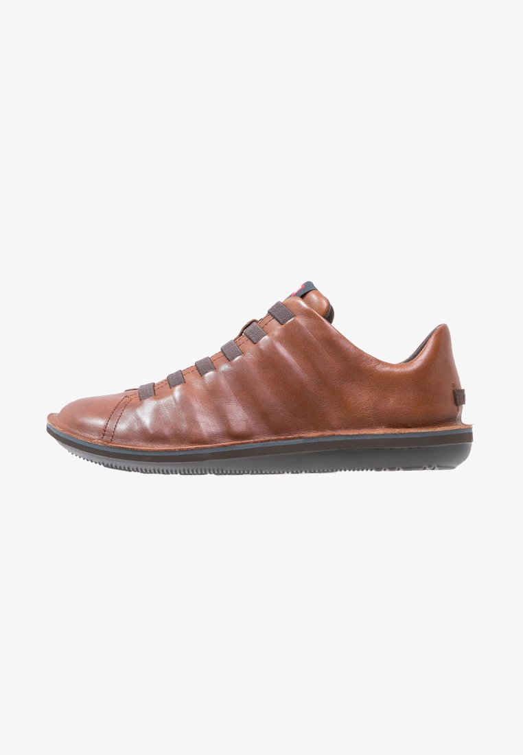 Sneaker en cuir marron avec des lacets élastiques, design épuré, semelle en caoutchouc, bout courbé et détails de couture minimaux.