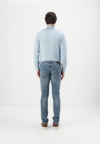 Camiseta de manga larga de color azul claro con un cuello alto, combinada con jeans de denim deslavados de corte ajustado y zapatos marrones, vista desde atrás.