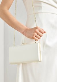 White acrylic clutch with a rectangular shape, gold chain strap, and a top clasp closure. Smooth surface, minimalistic design.