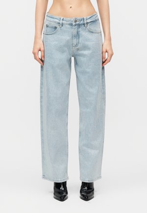 Λεπτή μέση με ανοιχτό μπλε, φαρδιά τζιν παντελόνια με λεπτό πουά μοτίβο, συνδυασμένα με μαύρα μποτάκια με μυτερή μύτη, πάνω σε απλό φόντο.