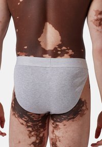 Szare bawełniane slipy z miękkim pasem, charakteryzujące się gładką teksturą. Skóra modela pokazuje wyraźne wzory ciemniejszych i jaśniejszych odcieni.