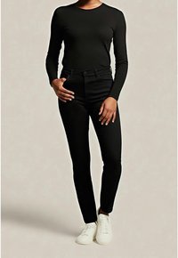 Černý top s dlouhými rukávy v kombinaci s černými přiléhavými džínami a bílými teniskami. Oblečení má jednoduchý design s hladkou texturou.
