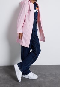 Jasnoróżowy płaszcz przeciwdeszczowy z kapturem, z zapięciem na guziki i bocznymi kieszeniami, noszony na granatowej koszulce i ciemnoniebieskich dżinsach. Białe trampki dopełniają całość.