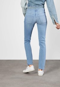 Jeans de denim azul claro con corte ajustado, diseño de cinco bolsillos, cinturilla estándar y un ligero desvanecimiento. Llevados con zapatillas blancas.