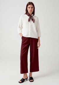 Woman wearing a white buttoned sweater, burgundy wide-leg pants, burgundy scarf tied at neck, and black heeled open-toe sandals.