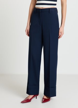 Pantalon bleu marine taille haute, coupe ample avec des plis marqués. Dispose de poches latérales et d'une texture de tissu lisse. Assorti à des talons rouges en cuir verni.