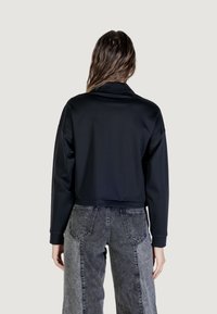 Felpa nera corta con una texture liscia, maniche larghe con polsini e colletto alto, abbinata a jeans grigi a vita alta.
