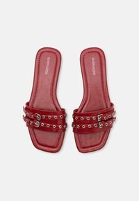 Red synthetic slide sandals with two wide straps featuring silver eyelets and buckles. Square toe design with flat soles and textured surface.