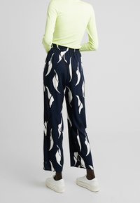 Marineblauwe wijde broek met een wit abstract bladpatroon, een elastische tailleband en zachte stof, gecombineerd met witte sneakers.