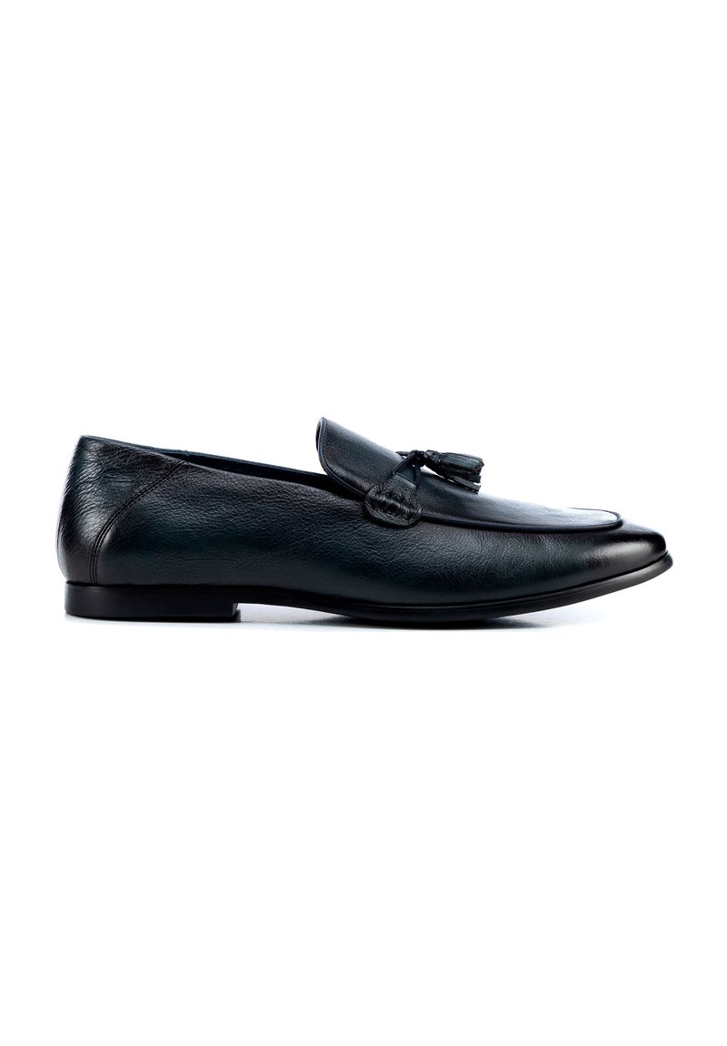 Los mocasines de piel negra presentan un acabado suave, una punta afilada y borlas decorativas en la parte superior. La suela es plana y de diseño sencillo.