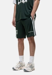 Zielone szorty sportowe o siateczkowej fakturze, z białymi paskami po bokach oraz napisem "GOODFORNOTHING". W zestawieniu z białymi skarpetkami i butami do biegania.