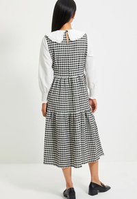 Svart och vit rutigt midi-klänning med rynkad krage, puffärmar, nyckelhål baktill och lagerkjol. Slät textur, avslappnad design.
