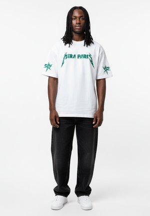 Witte t-shirt met korte mouwen en groene "PARIS" grafische print en sterrenontwerp op de mouwen, gecombineerd met donkerdenim jeans en witte sneakers.