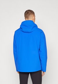 Veste imperméable bleue avec capuche intégrée, texture lisse et coupe droite, présentant un design uni sans embellissements visibles.
