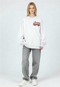 Sweat-shirt gris avec "Amour" brodé en rouge, associé à un jean gris ample et des baskets blanches. Tissu doux, coupe décontractée et manches longues.