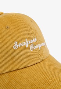 Gorra de pana amarilla con el texto bordado en blanco "Scalpers Company". Cuenta con un tejido texturizado, visera curvada y detalles cosidos.