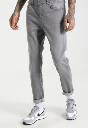 Vaqueros de denim gris claro con un corte slim, dobladillos enrollados y bolsillos delanteros, combinados con zapatillas Nike blancas y grises, con detalles en negro.