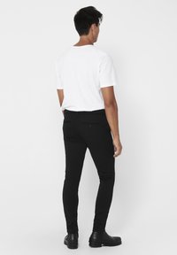 Zwarte aansluitende broek met een gladde textuur, achterzakken en standaard riemlussen. Gemaakt met een eenvoudig wit T-shirt en zwarte laarzen.
