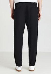 Pantalons noirs à la texture lisse, avec des poches arrière et une coupe ajustée. Les ourlets roulés laissent apparaître des baskets blanches avec une semelle contrastante.
