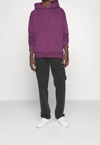 Paarse hoodie met een voorzak, gecombineerd met donkergrijze broek en witte sneakers. Gladde textuur, casual ontwerp.