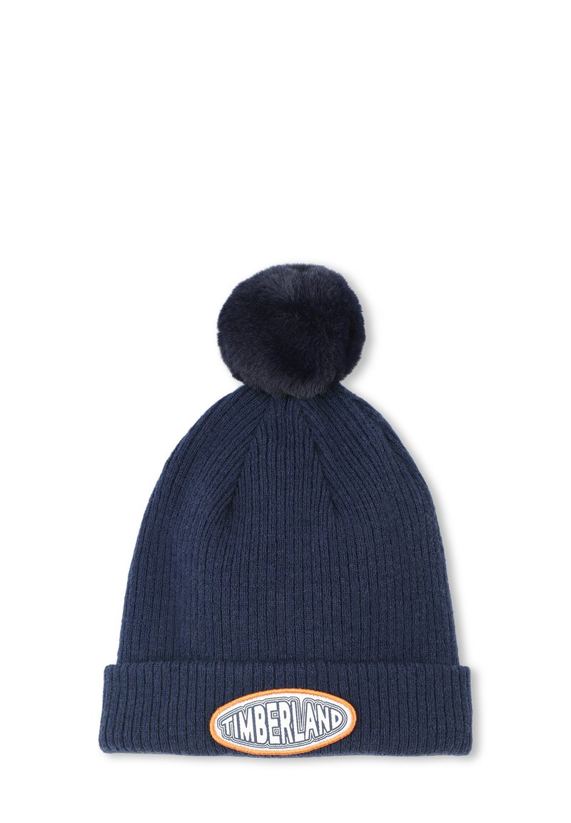 Beanie lavorato a maglia di colore navy con un design a coste testurizzato e un grande pompon in pelliccia sintetica sulla parte superiore. Presenta una prominente etichetta con il logo Timberland sulla parte frontale.