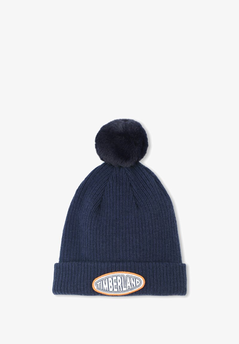 Beanie lavorato a maglia di colore navy con un design a coste testurizzato e un grande pompon in pelliccia sintetica sulla parte superiore. Presenta una prominente etichetta con il logo Timberland sulla parte frontale.