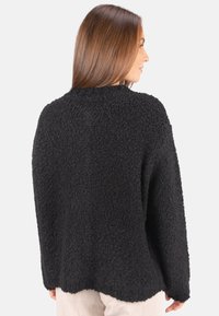 Schwarzer, strukturierter Pullover mit lässigem Schnitt, überschnittenen Schultern und Rundhalsausschnitt. Der Stoff wirkt weich und flauschig, mit abgerundetem Saum.