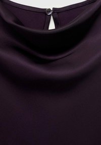 Fialová blůza se soft drapovanou tkaninou, vysokým výstřihem a knoflíkovým zapínáním na zadní straně. Hladká textura s jemným leskem.