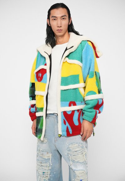 Barvna flis jakna s kapuco, ki vsebuje abstraktne nalepke v rdeči, rumeni, zeleni in modri barvi. Okrašena z belimi obrobami in zadrgo.