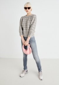 Grå stickad tröja med strukturerade mönster, blå jeans, rosa handväska och ljusgrå sneakers. Modell med mörka solglasögon.