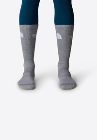 Calcetines grises hasta la rodilla con textura acanalada, talones reforzados y el logo de North Face en blanco en el puño. Material de tela suave.