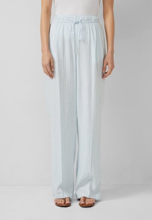 Jasnoniebieskie szerokie spodnie z białymi pionowymi paskami, w pasie ze sznurkiem, noszone z białym topem i brązowymi płaskimi sandałami.