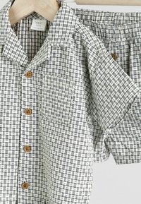 Kurzarmpoly-Shirt und Short-Set aus Baumwolle, mit einem schwarz-weißen Karomuster, Holzknöpfen und einer Brusttasche. Elastischer Bund an den Shorts.