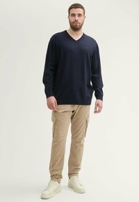 Marineblauer V-Ausschnitt-Pullover aus weichem Stoff, kombiniert mit hellen khakifarbenen Cargo-Hosen mit Seitentaschen und beigen Sneakers. Einfaches Design und lockere Passform.